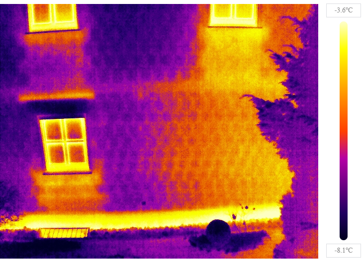 Titelbild des Blogbeitrages. Zusehen ist ein Haus, aufgenommen mit einer Infrarotkamera. Erklärung: Helle Stellen in der Thermographie-Aufnahme deuten auf unzureichende Isolierung an Sockel, Heizkörpernische, Fenster und Rollo Kasten hin.