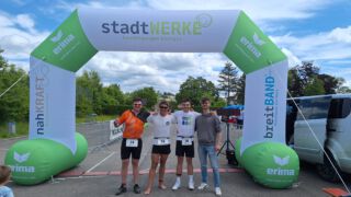 Marco Obermeier, Gerd Hofmann, Thomas Haupt und Kevin Settler beim Feuchtwanger Triathlon. Zusammen stehen sie vor dem Ziel und lächeln in die Kamera.